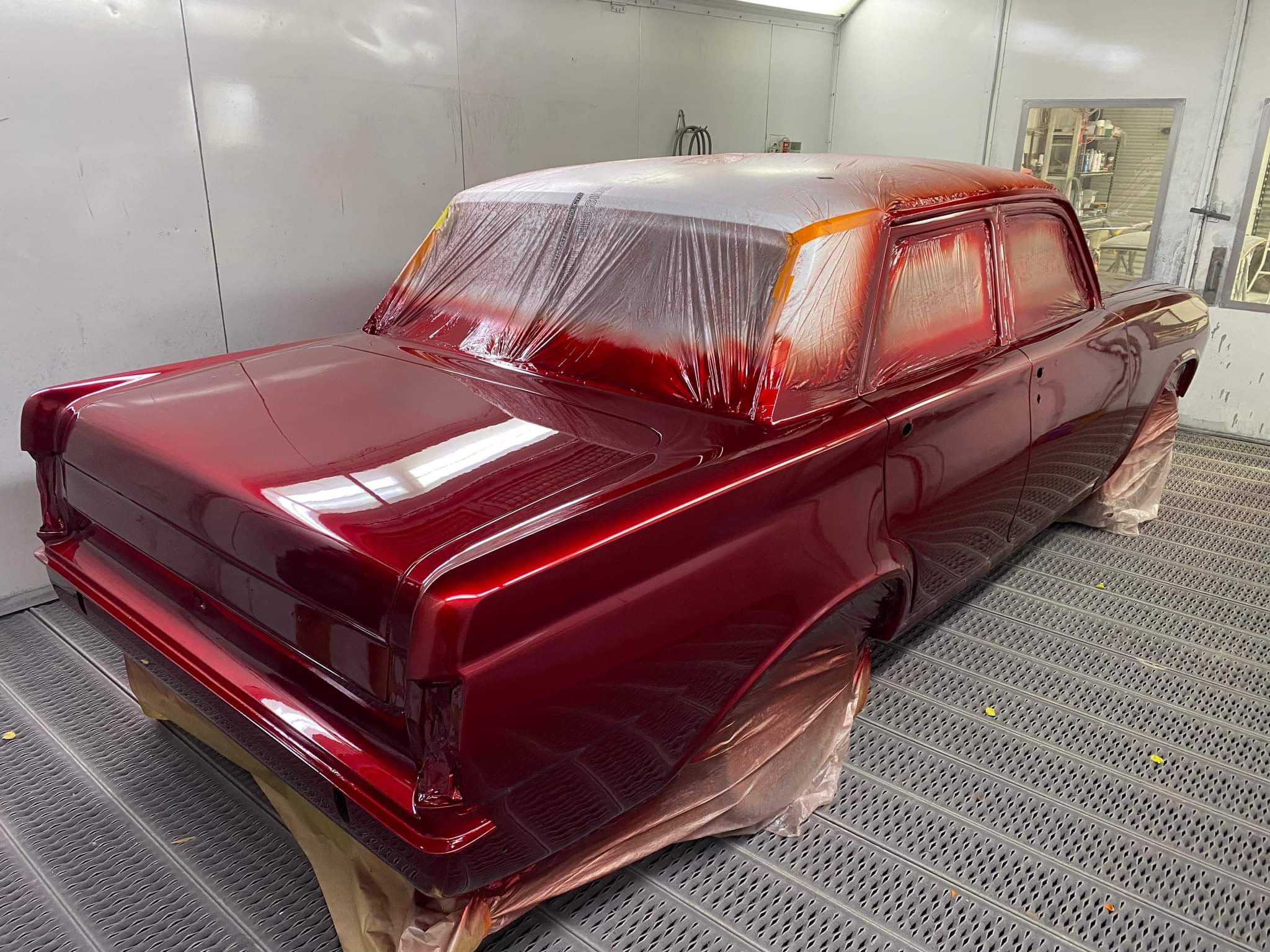 A classic sedan shell in deep candy red, masked up on the grating inside the spray booth