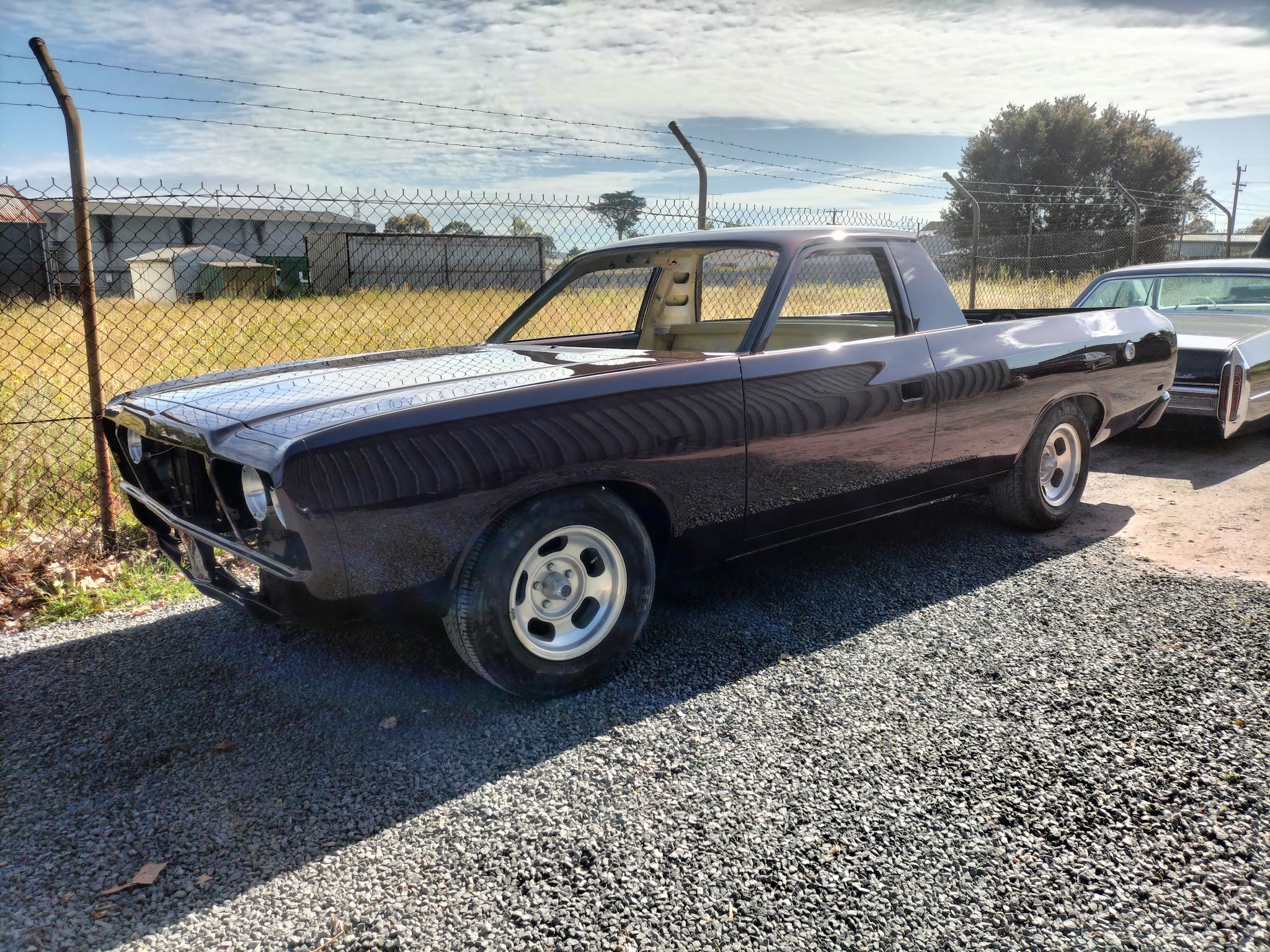 A deep plum Valiant ute finished and parked in the sun beside a Cadillac