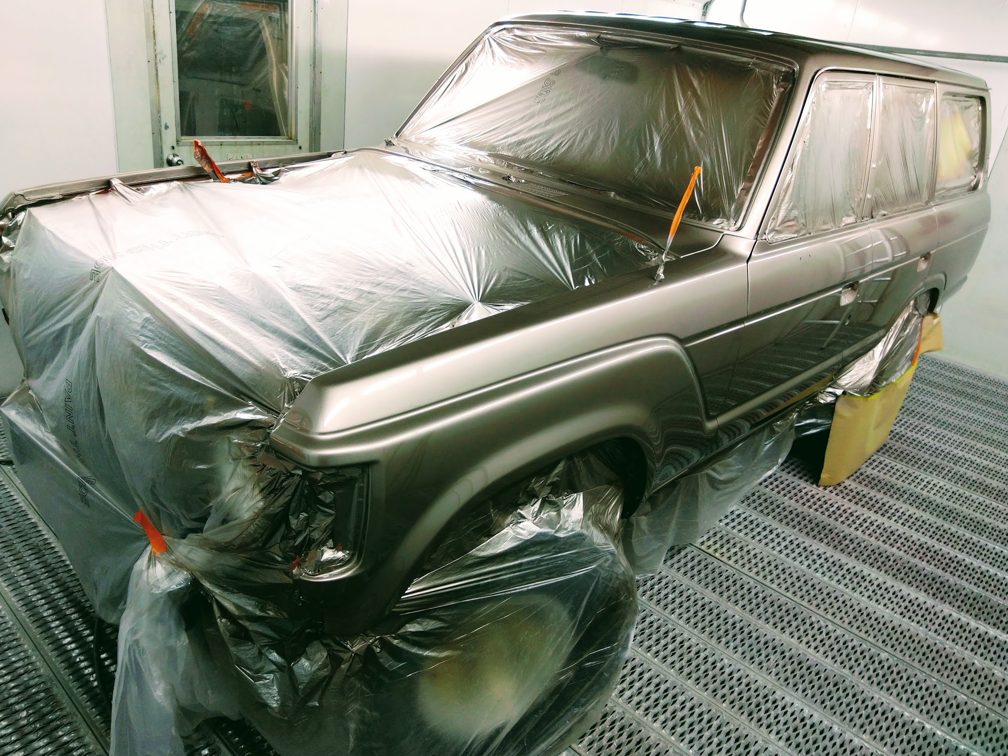 A four wheel drive wagon in fresh gunmetal, masked and sheeted in the booth