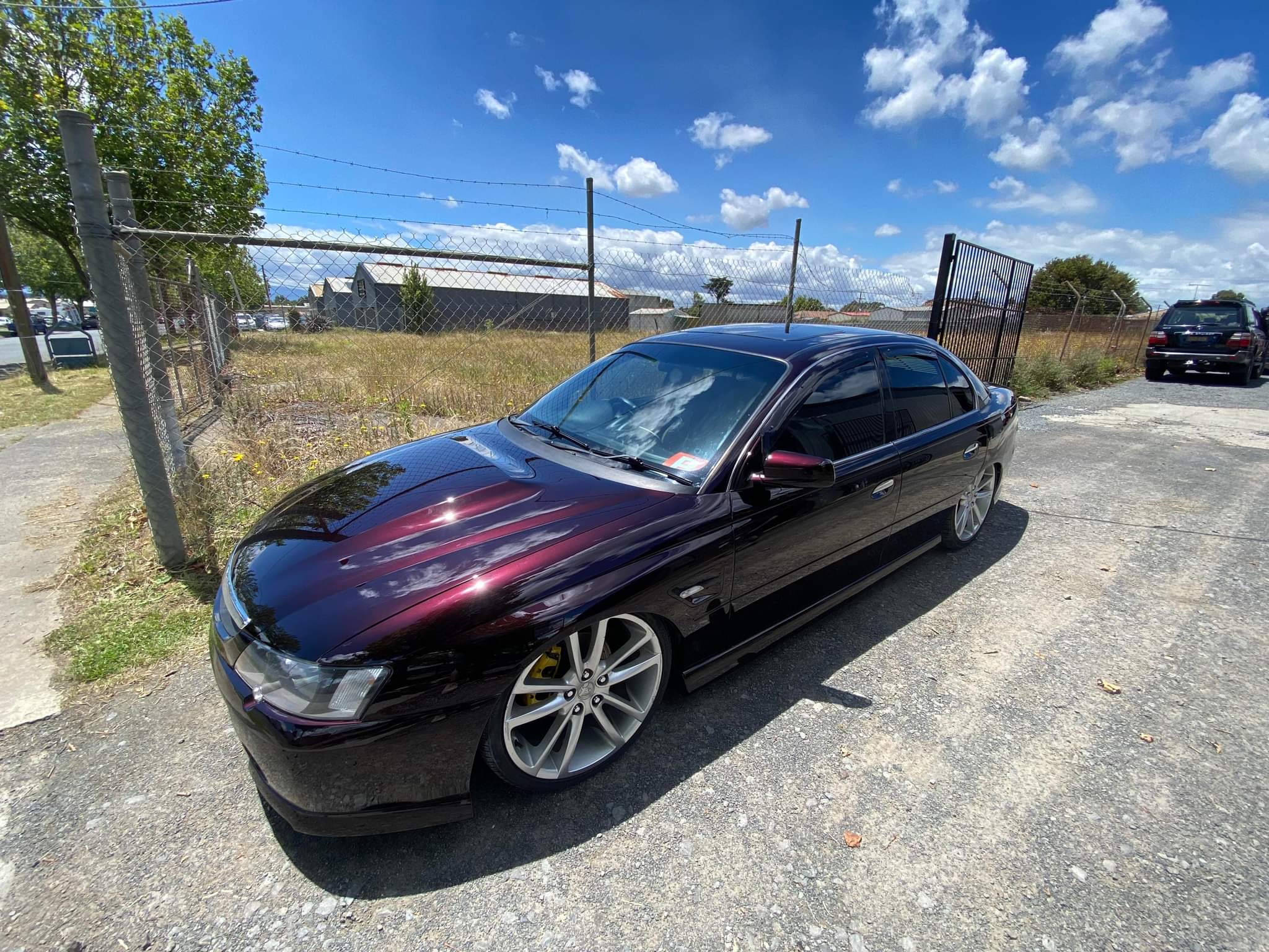 A finished Holden Commodore in deep purple black cherry, parked outside the workshop under a blue sky